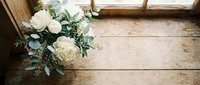 White roses and eucalyptus wedding bouquet on rustic wooden floor near window with natural light for bridal photography and romantic celebrations.