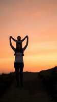 Father carrying child on shoulders silhouetted against warm sunset sky creating heartwarming family bonding moment outdoors.