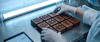 Professional chocolatier in white gloves crafting artisan chocolate squares with intricate patterns in modern kitchen workspace for gourmet confectionery production.
