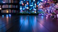 Wooden floor with blurred bokeh lights and purple flowers in foreground creating dreamy atmosphere. Dark moody interior with blue glowing background.
