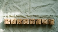 Wooden letter blocks spelling PRACTICE arranged in row on crumpled paper background for education training skill development concepts.