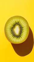 Fresh kiwi fruit half with vibrant green flesh and black seeds on bright yellow background, casting strong shadow for food photography.