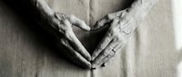 Elderly hands forming a heart shape on linen fabric, black and white close-up symbolizing love, care, and wisdom in aging.