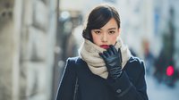 Young Asian woman in winter coat and scarf walking through urban city street with thoughtful expression during cold weather season.