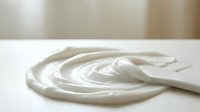 Creamy white swirl of thick yogurt or sour cream with smooth texture on clean surface, perfect for food photography and culinary designs.