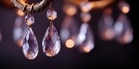 Elegant crystal drop earrings with faceted teardrop pendants hanging from gold-toned hooks against warm bokeh background for luxury jewelry display.