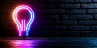 Glowing neon light bulb against dark brick wall background with pink and blue reflection on floor, creative innovation concept for business solutions.