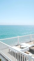 Serene ocean view from white wooden deck with lounge chairs overlooking turquoise water and clear blue sky for vacation relaxation and coastal living.