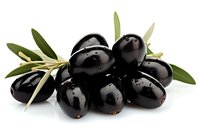 Fresh black olives with green leaves and water drops on white background, macro food photography for Mediterranean cuisine and healthy eating concepts.
