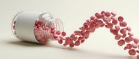 Pink capsules spilling from white medicine bottle creating flowing stream on neutral background for healthcare and pharmaceutical concepts.