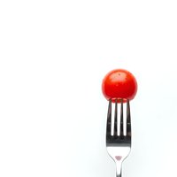 Red cherry tomato on fork isolated on white background for healthy eating and cooking concepts.