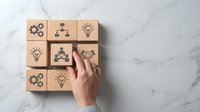 Hand arranging wooden blocks with business innovation icons including lightbulbs, gears, and network symbols on marble surface for strategic planning.