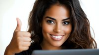 Young woman with bright smile showing thumbs up gesture while looking at camera, expressing positivity and approval. Professional headshot for business or marketing.