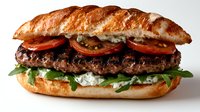 Gourmet burger with arugula, tomatoes and cream sauce on artisanal bread roll, close up view against light background. Fresh homemade sandwich.