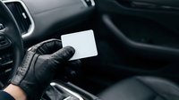Close-up of hand wearing black leather gloves holding blank white card inside modern car interior. Suitable for business, automotive, and promotional material concepts.