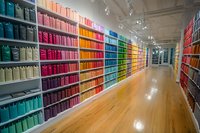Long corridor with colorful rainbow-arranged storage boxes on shelves, wooden floor reflecting bright overhead lights, organized retail display in modern interior.