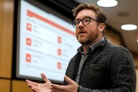 Professional businessman with glasses presenting data analytics on screen during corporate meeting or conference in modern office environment.