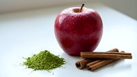 Red apple with cinnamon sticks and matcha powder on white surface, fresh fruit and spices for cooking, baking, wellness and culinary design projects.