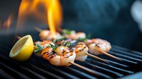 Grilled jumbo shrimp on barbecue with rosemary herbs and lemon slice, flames and smoke in dark moody background. Fresh seafood cooking on hot grill.
