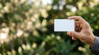 Man holding blank white business card outdoors with blurred green foliage background, suitable for branding and corporate marketing materials.