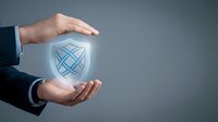 Male hand in business suit protecting glowing shield icon with checkmark symbol, representing data security, protection, and trust for corporate safety concepts.