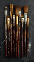 Old well-used artist paintbrushes with wooden handles and natural bristles arranged vertically on dark textured background, showing wear and creative character.