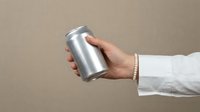Hand holding blank aluminum beverage can mockup against neutral beige background for branding and packaging design projects.