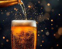 Golden beer pouring into glass with foam head against dark background with bokeh lights, creating splashes and bubbles.