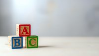 Colorful wooden alphabet blocks with letters A, B, C stacked in pyramid formation on white surface against neutral background for educational content.