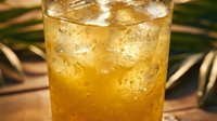 Refreshing iced golden cocktail in a glass with crushed ice, tropical palm leaves in background, summer drink concept.