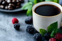 Fresh black coffee in ceramic cup with ripe blackberries, raspberries and mint leaves on gray concrete background, selective focus with blurred chocolate.