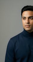 Young South Asian male wearing navy turtleneck against neutral gray background. Professional headshot suitable for corporate profiles, business websites, and professional networking platforms.