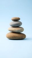 Balanced stack of four smooth river stones arranged in zen tower formation on clean light blue background representing mindfulness and inner peace.
