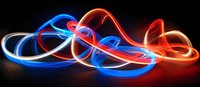 Glowing neon light trails in red, blue and white colors create dynamic swirling pattern against black background, abstract long exposure light painting effect.