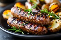 Grilled sausages with roasted potatoes and fresh rosemary on black plate, close up view. Juicy meat with golden crust and herbs for restaurant menu.