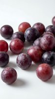 Fresh ripe plums scattered on white background showing natural purple and red colors with glossy skin texture for healthy eating and cooking concepts.