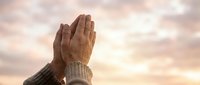 Hands raised in prayer against soft sunset sky with warm golden light. Spiritual worship moment expressing faith, gratitude and devotion in peaceful atmosphere.