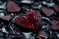 Red heart-shaped object with water droplets on dark wet surface surrounded by scattered heart shapes for romantic Valentine's Day concepts.