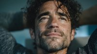 Close-up portrait of exhausted Hispanic man with curly hair and beard showing fatigue after intense workout or physical activity in gym setting.