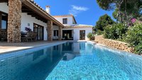 Mediterranean villa with stone facade and turquoise swimming pool surrounded by lush garden landscape. Covered terrace offers shaded outdoor living space on sunny summer day.