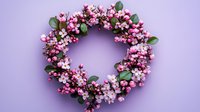 Pink spring blossom wreath with eucalyptus leaves arranged in circle shape on purple background, festive floral decoration for seasonal celebrations.