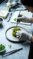Chef in white gloves plating gourmet vegetable dish with tweezers on marble counter, professional kitchen preparation and fine dining food presentation.