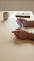 Hands interacting with transparent holographic display technology on wooden desk with coffee cup and notebook in modern workspace for futuristic interface design.