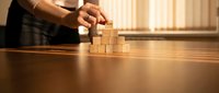 Businessman hands carefully stacking wooden blocks on office desk, representing strategic planning, growth, and building success in corporate environment.