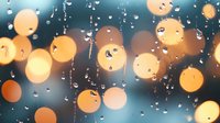 Glowing golden bokeh lights with water drops on glass creating magical atmosphere. Blurred circles and raindrops pattern on window at night.