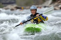 Female kayaker navigating through white water rapids in bright green kayak with paddle, wearing safety helmet and life vest for adventure sport.