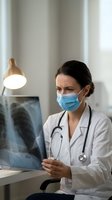 Female doctor in medical mask examining chest x-ray in modern clinic office. Healthcare professional analyzing patient radiograph for diagnosis and treatment.