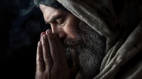 Bearded senior man in hooded robe praying in dark atmospheric setting with dramatic lighting and rising smoke, spiritual contemplation and faith concept.
