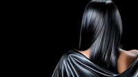 Young Asian woman with long straight black glossy hair from behind wearing black silk dress against dark background, beauty and haircare concept.