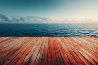 Wooden deck or pier overlooking calm blue ocean waters at sunset with dramatic sky and horizon, perspective view of natural wood planks in warm tones.